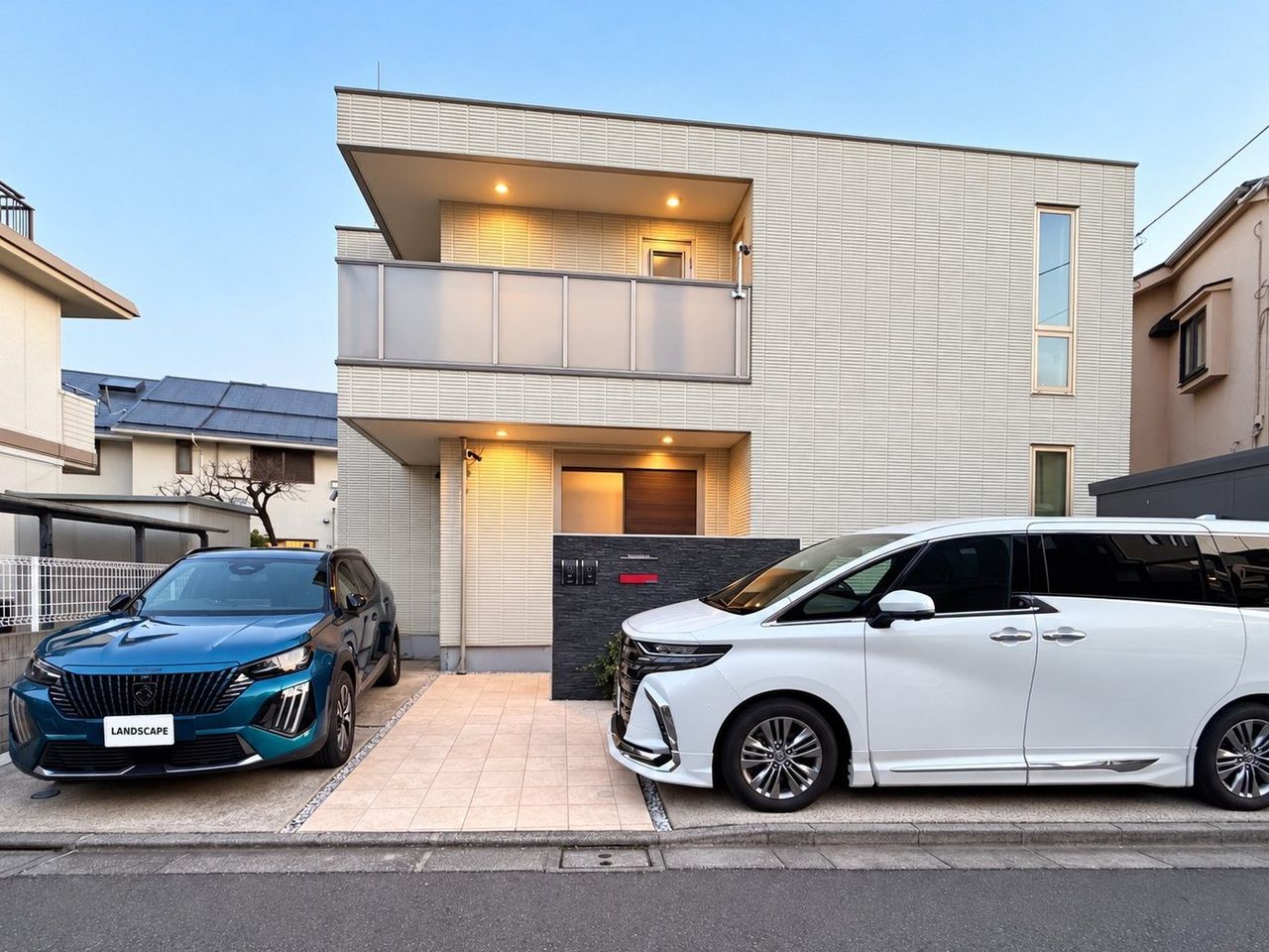 夕暮れの一戸建てと、駐車場の2台の車
